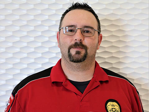 A portrait of a bearded man wearing glasses in a red and black shirt.