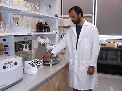 A researcher in a lab coat stands next to a counter filled with biotechnology equipment.