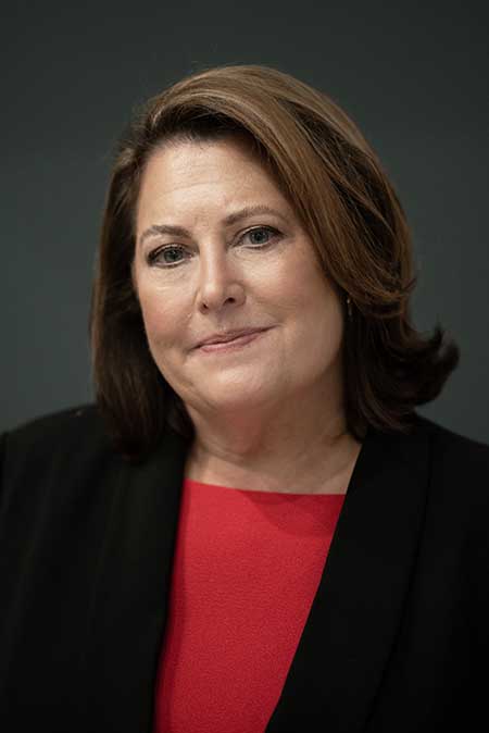 Portrait of woman in a black suit jacket and red shirt.