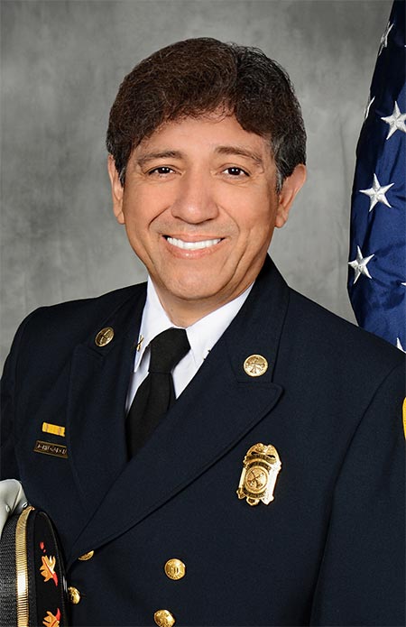 A Hispanic man smiling in a formal fire marshal uniform.