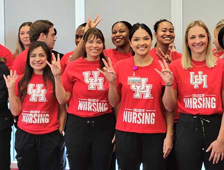A group of nursing students stand together in red shirts holding their right hangs in a cougar paw sign.