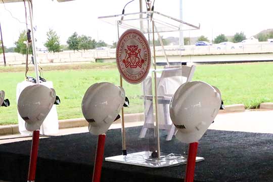 A close up of a glass podium with the UH presidential seal on the front. Shovel handles are visible in the foreground.