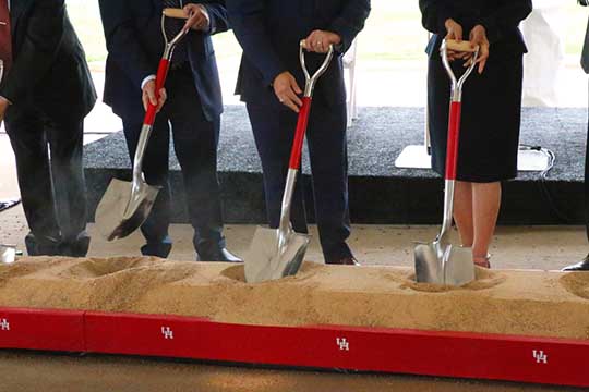 A closeup of three shovels in a small mound of dirt. Three people have placed the hands in the shovel handles.