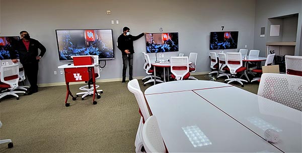 Groups of white tables with wall-mounted monitors surround a moveable podium.