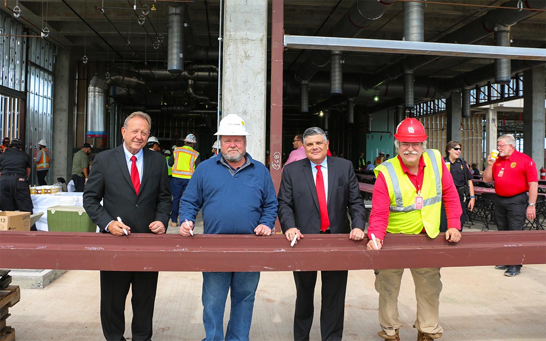Two men in suits and two men in construction outfits signing a metal girder