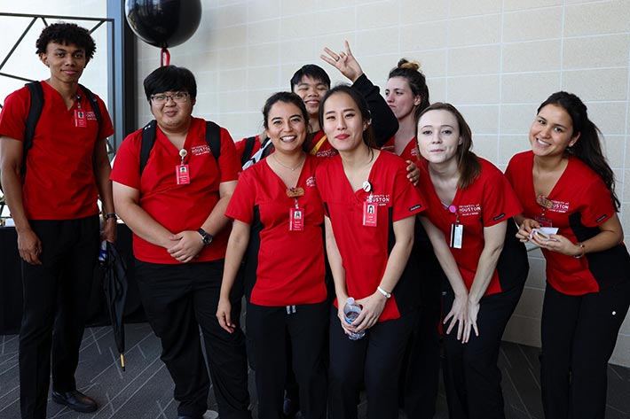A group of diverse students in red and black nursing scrubs