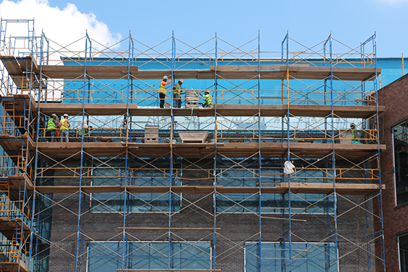 Constructions workers on scaffolding covering the side of a brick building