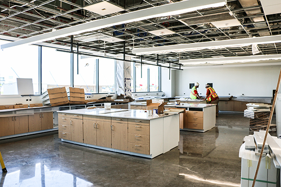 Construction workers installing tables with drawers and cabinets in an unfinished lab