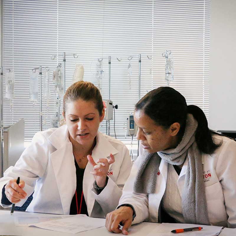 Two nursing faculty work together at a desk in a nursing lab.
