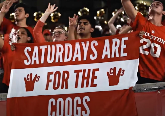 Students at a TDECU Stadium game cheer on the Coogs while holding a flag that says, 