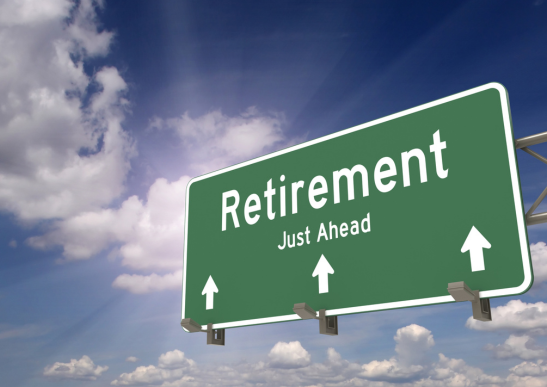 Image of a green highway sign that says retirement just ahead with a blue sky and clouds behind it.