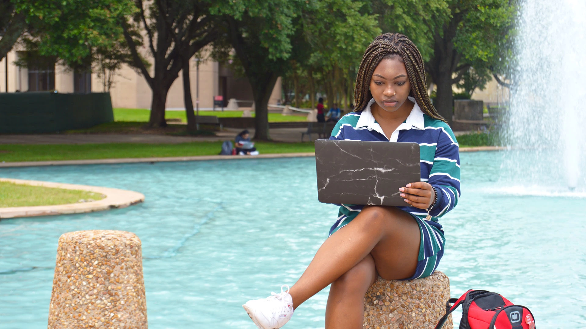 A student on her laptop in front of the fountains.