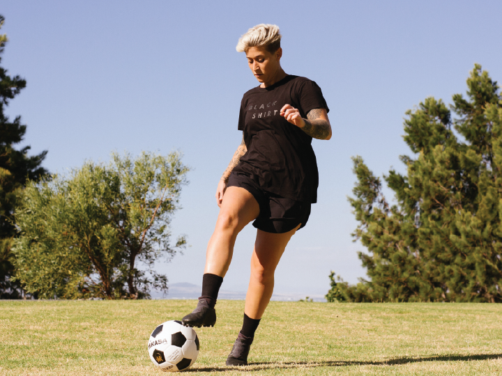 Woman with short platinum blonde hair dribbles a soccer ball in a field